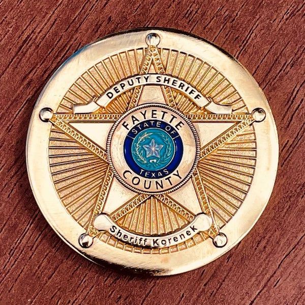 photo of polished gold challenge coin belonging to the Fayette County Texas Sheriff Korenek sitting on a wood table top