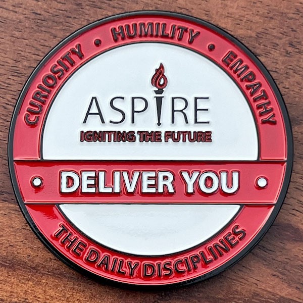 Round Challenge Coin belonging to Aspire. Red highlights, white background black and white letters.