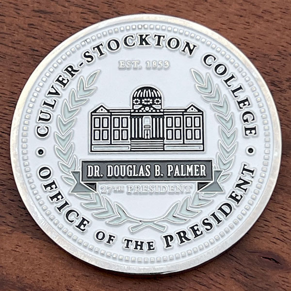 A round silver challenge coin representing the Culver-Stockton College President. 