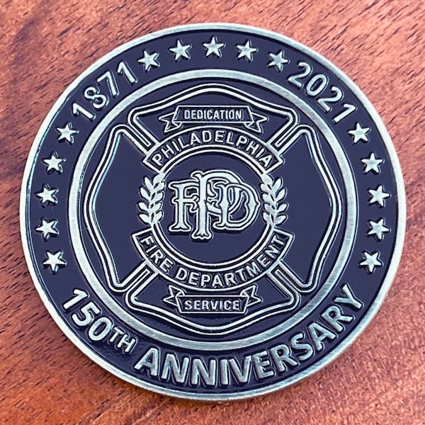 A round silver challenge coin representing the Philadelphia Fire Department. 