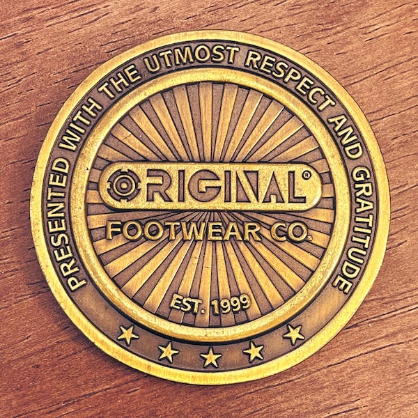 photo of antiqued gold challenge coin from the Original Footwear Company on a wooden table top