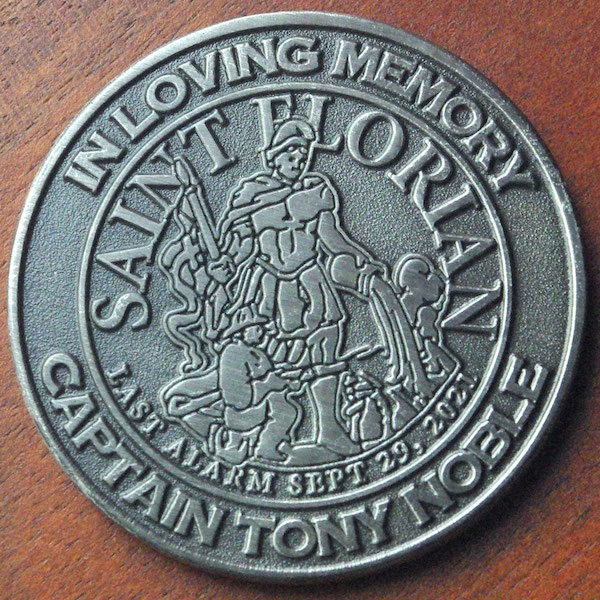 A round antique silver memorial challenge coin honoring Captain Tony Noble. 