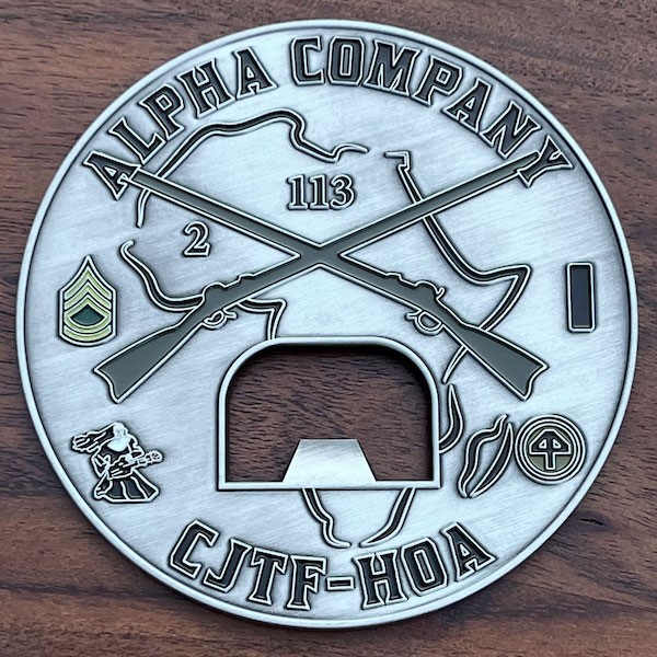 Round silver coin with cutout bottle opener center.Crossed rifles over Africa shihouette. Sgt. insignia, above nun with rifle.