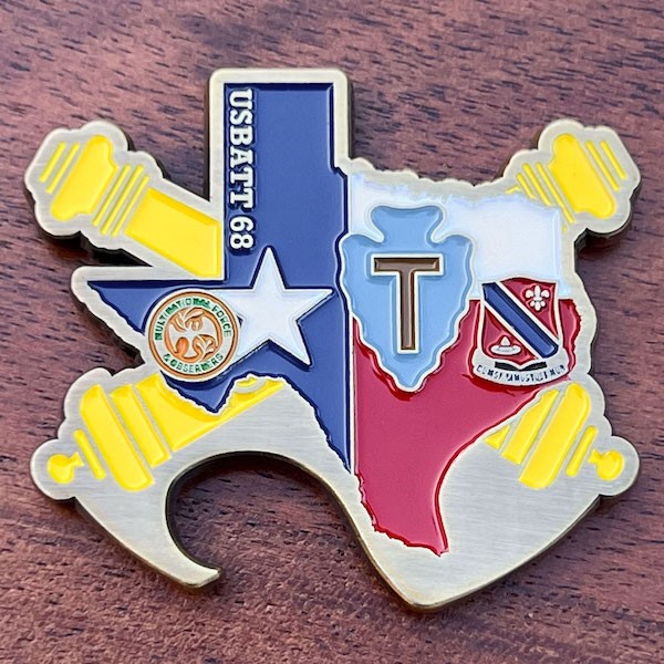 Texas-shaped coin with red, yellow, light and dark blue  highlights. Bottle opener on lower left edge