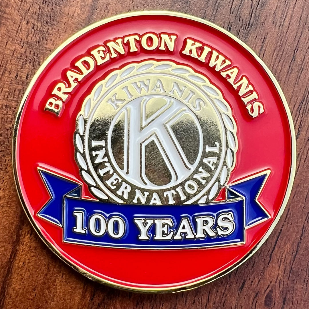 Round coin, red background, blue, white and gold lettering commemorating the Bradenton Kiwanis 100 Years