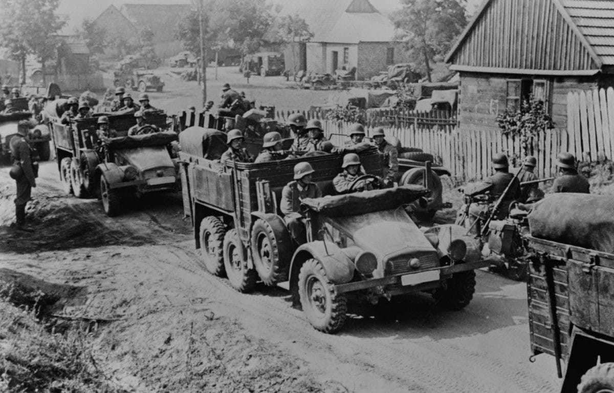 picture of troops rolling into a village in trucks during World War II
